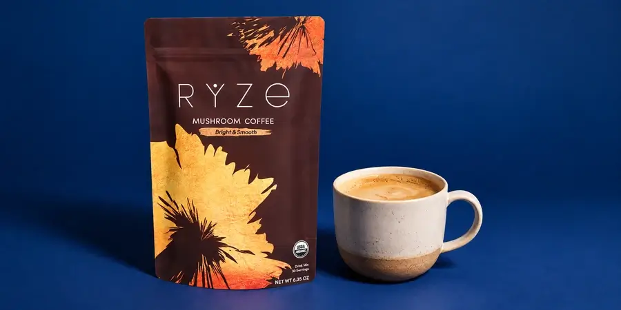 Confezione di RYZE Mushroom Coffee accanto a una tazza di caffè su sfondo blu notte